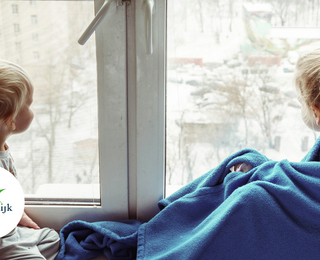Twee kinderen voor het raam met een dekentje