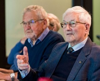 twee oudere mannen die aan tafel zitten