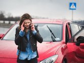 Vrouw staat naast rode auto te bellen