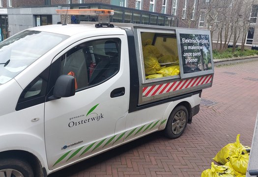 Auto van de gemeente met volle afvalzakken achterin