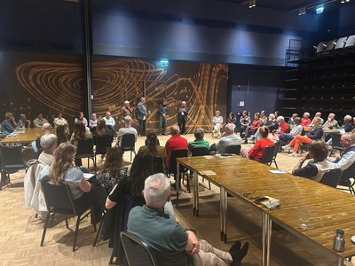 Veel mensen in een zaal die naar een paar sprekers kijken