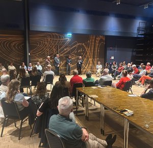 Veel mensen in een zaal die naar een paar sprekers kijken